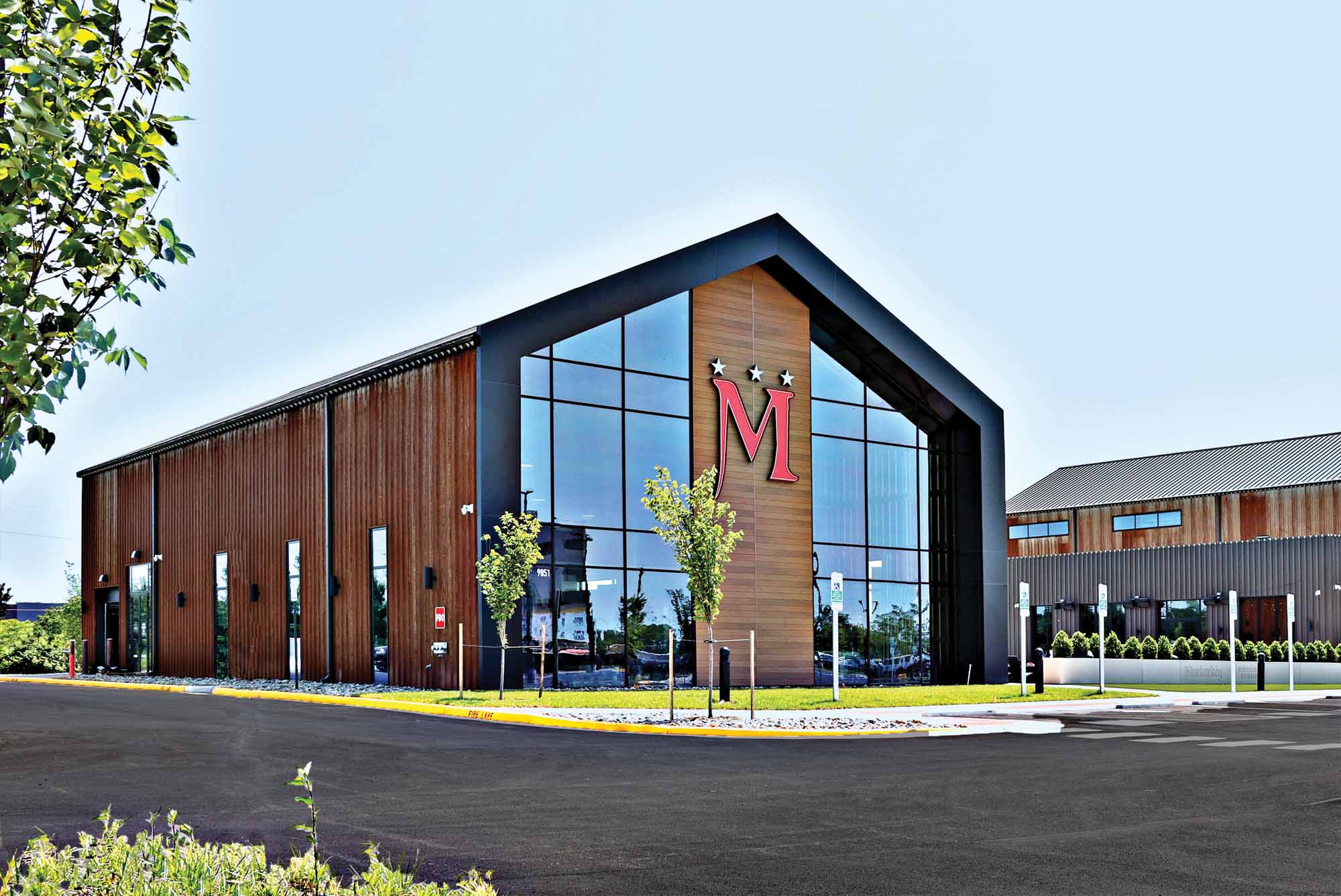 Contemporary community building with warm wood-tone siding, expansive glass entry and bold black metal framing beneath a bright blue sky.