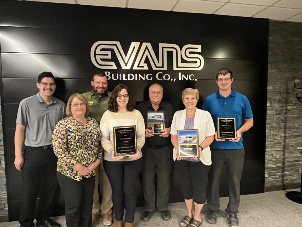 Evans Building Co. team members holding award plaques in front of company sign.