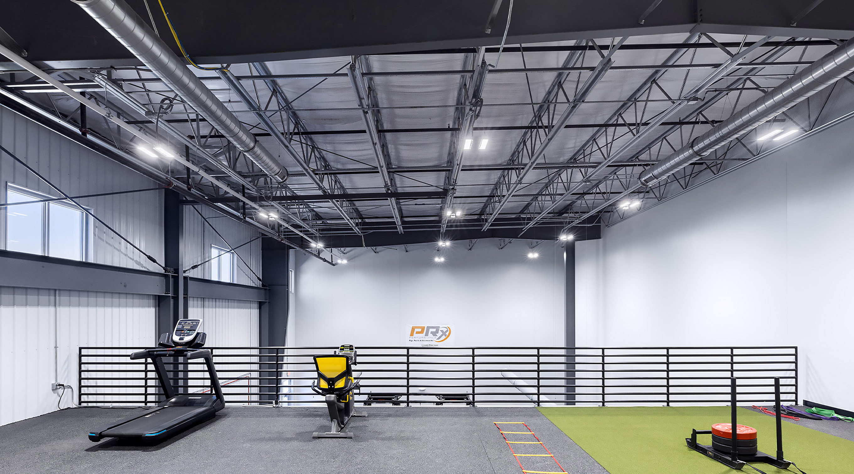 Industrial warehouse interior with storage racks, mezzanine level, and small indoor basketball court area on polished concrete floor.