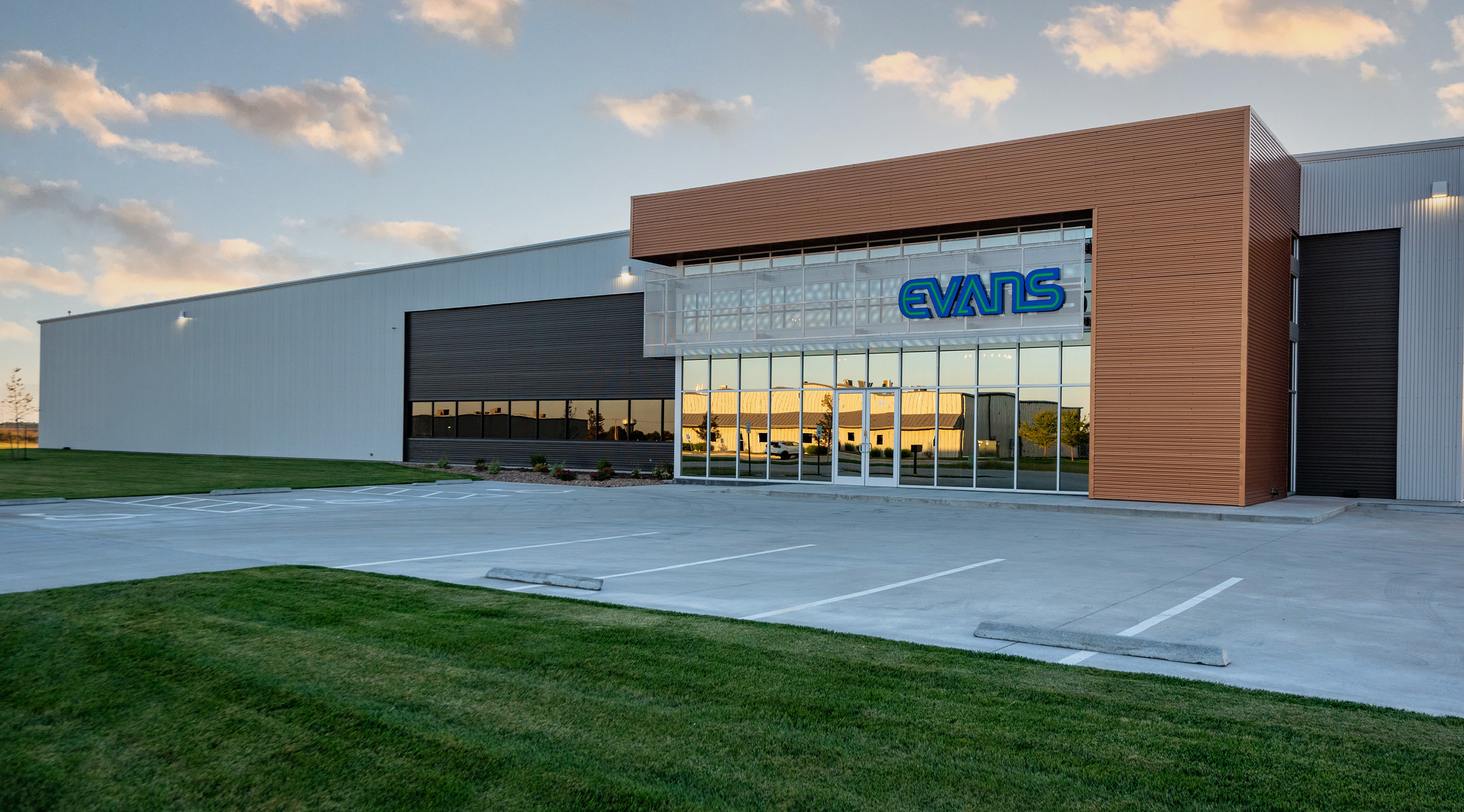 Modern commercial building with glass storefront and metal exterior panels at sunset.