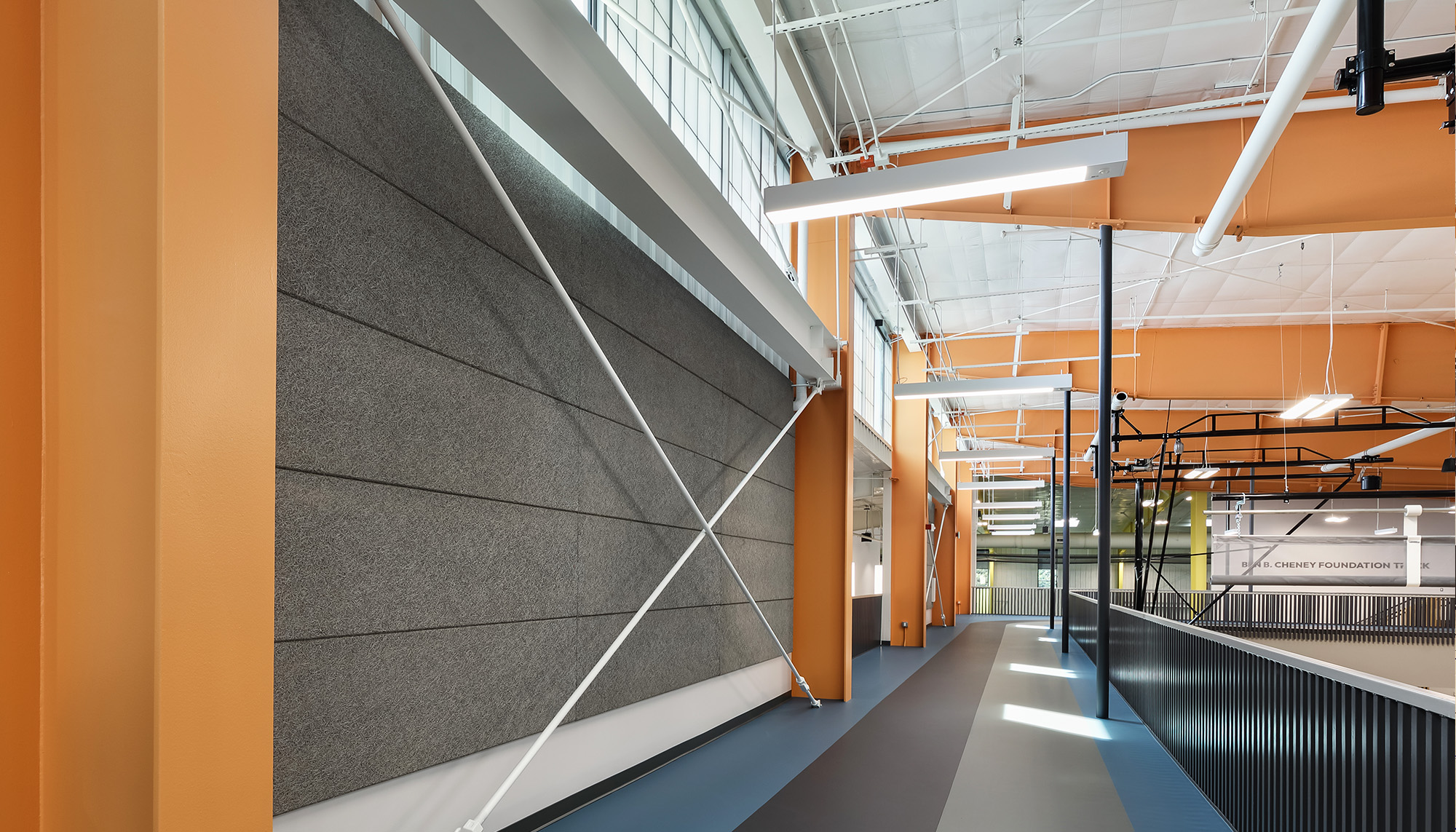 Contemporary interior corridor with warm orange structural framing, acoustic wall panels and exposed steel detailing designed for collaborative gathering spaces.