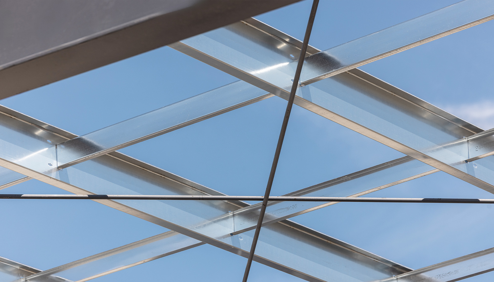 Close-up view of exposed steel roof framing and cross-bracing against a clear blue sky, highlighting engineered structural support systems.