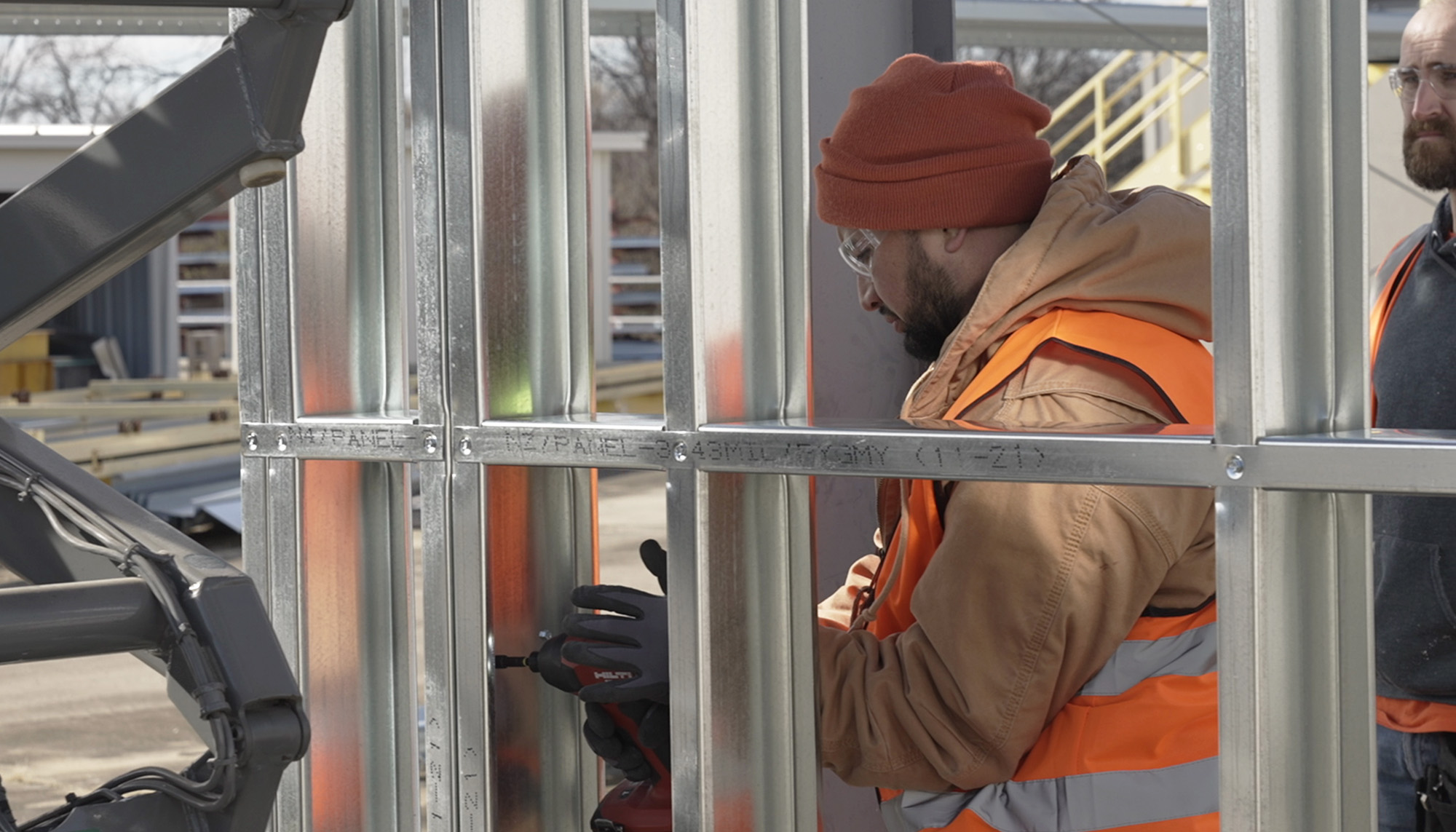 Construction worker in a safety vest securing metal wall framing at an active building site.