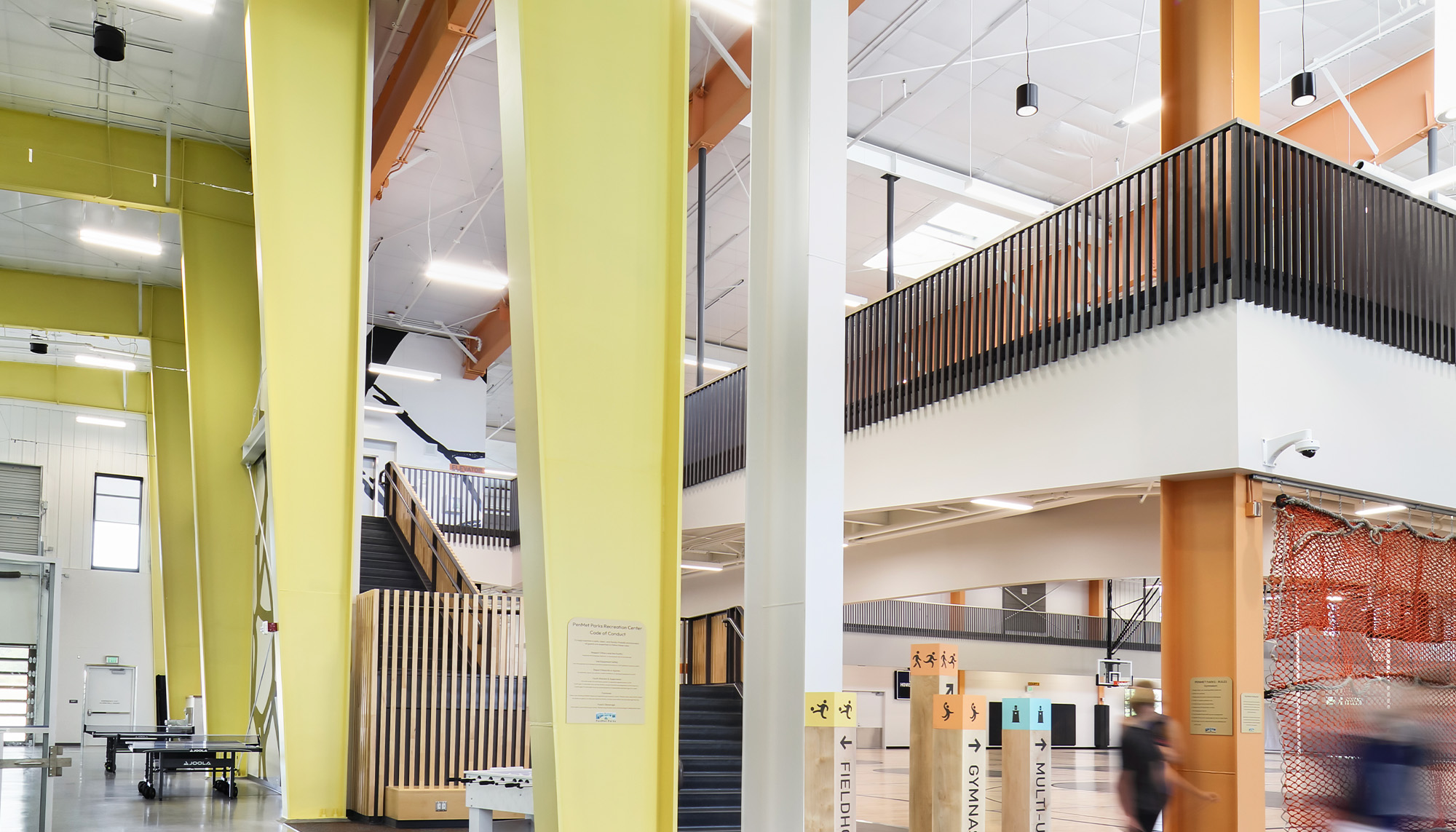 Bright contemporary interior with lime green structural columns, open mezzanine walkways and collaborative gathering spaces designed for active community use.