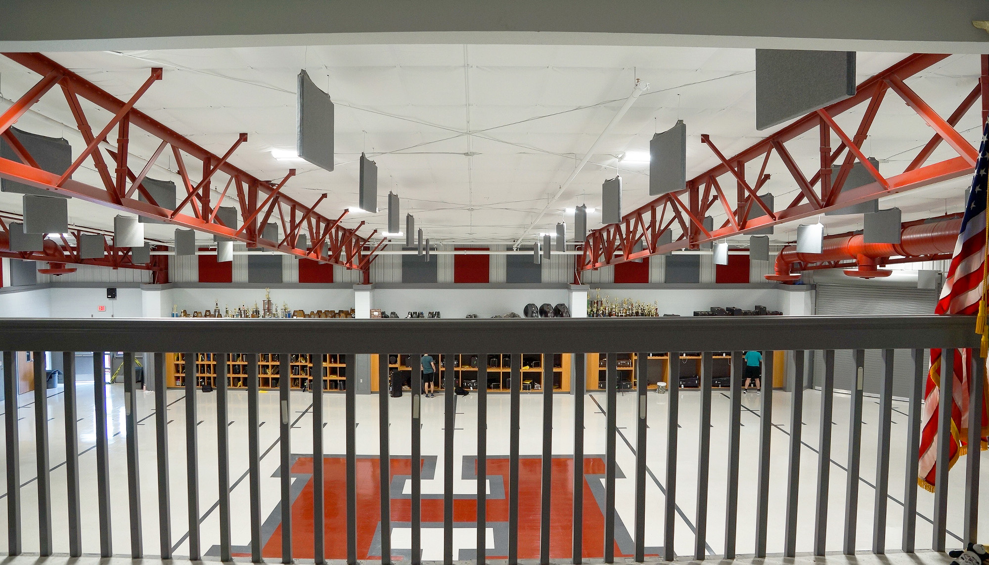 Interior athletic facility with exposed red steel trusses, open mezzanine railings and multi-level training courts viewed from an upper concourse.