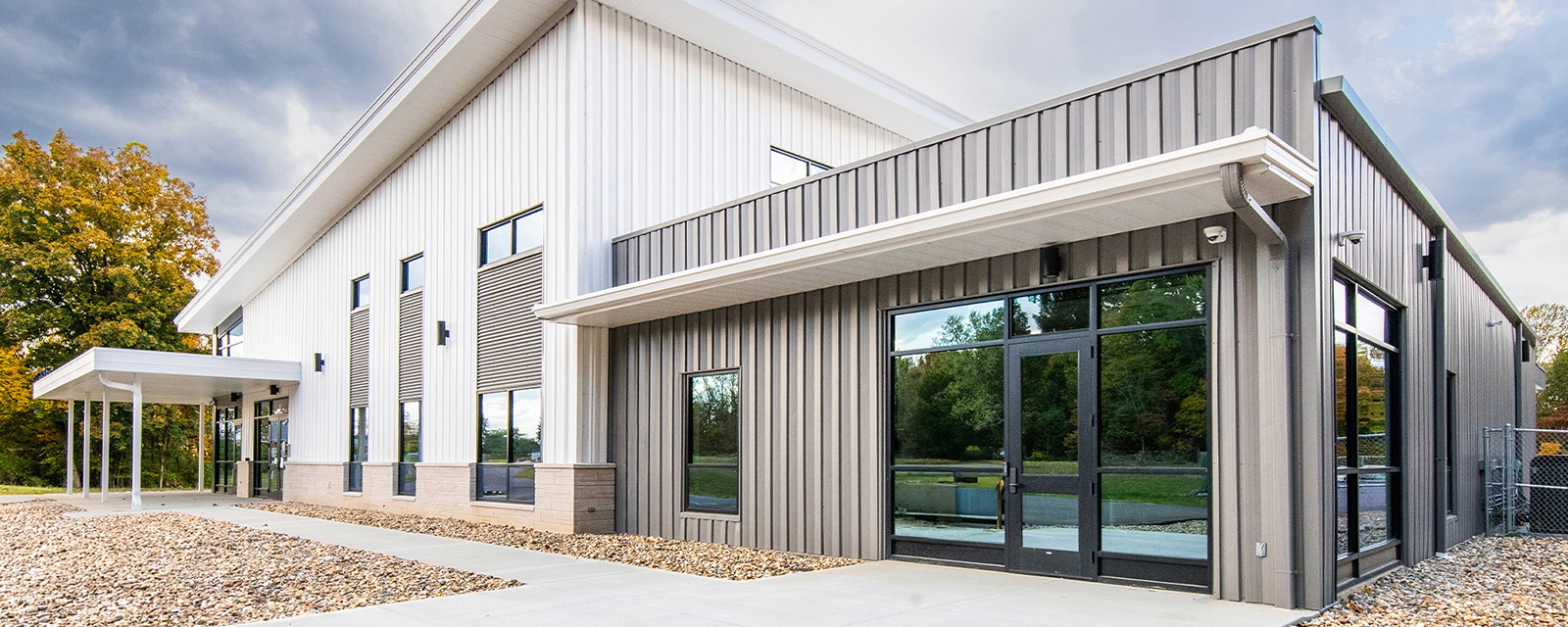 Contemporary white metal building with vertical panel cladding, expansive glass storefront and clean architectural lines set within a landscaped campus environment.