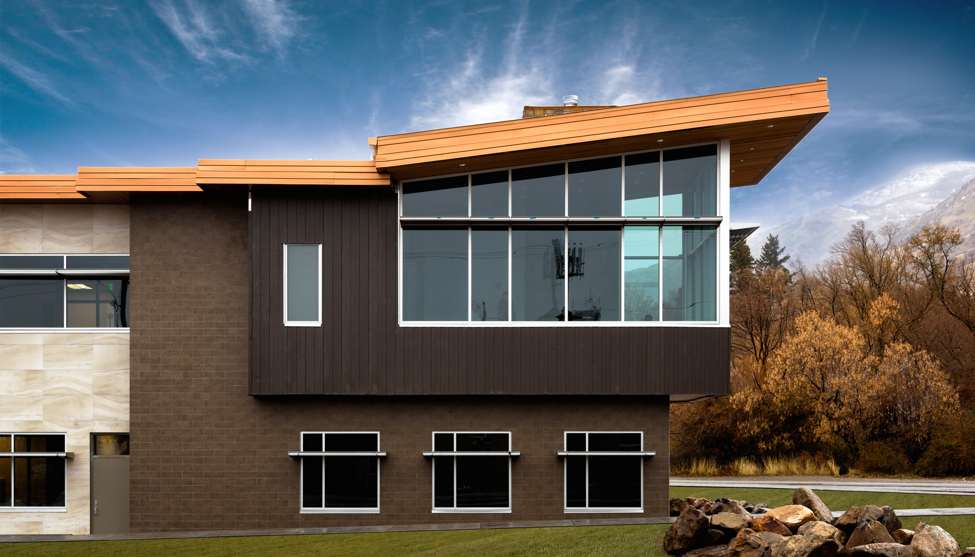 Modern two-story commercial building with brick and metal façade, large glass windows and extended roof overhang.