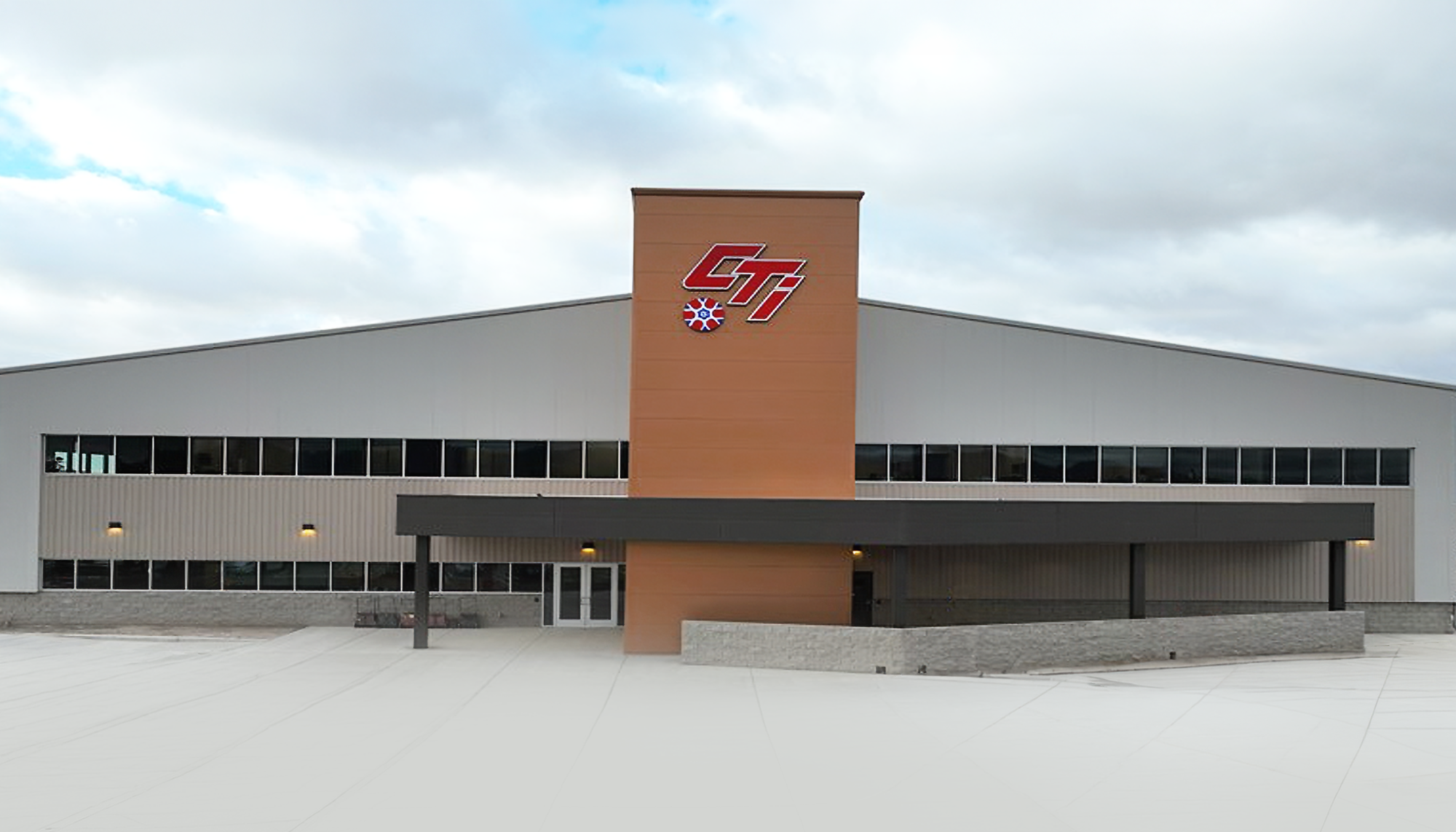 Large light-gray metal commercial building with central entry tower, covered drop-off area and wide concrete apron.