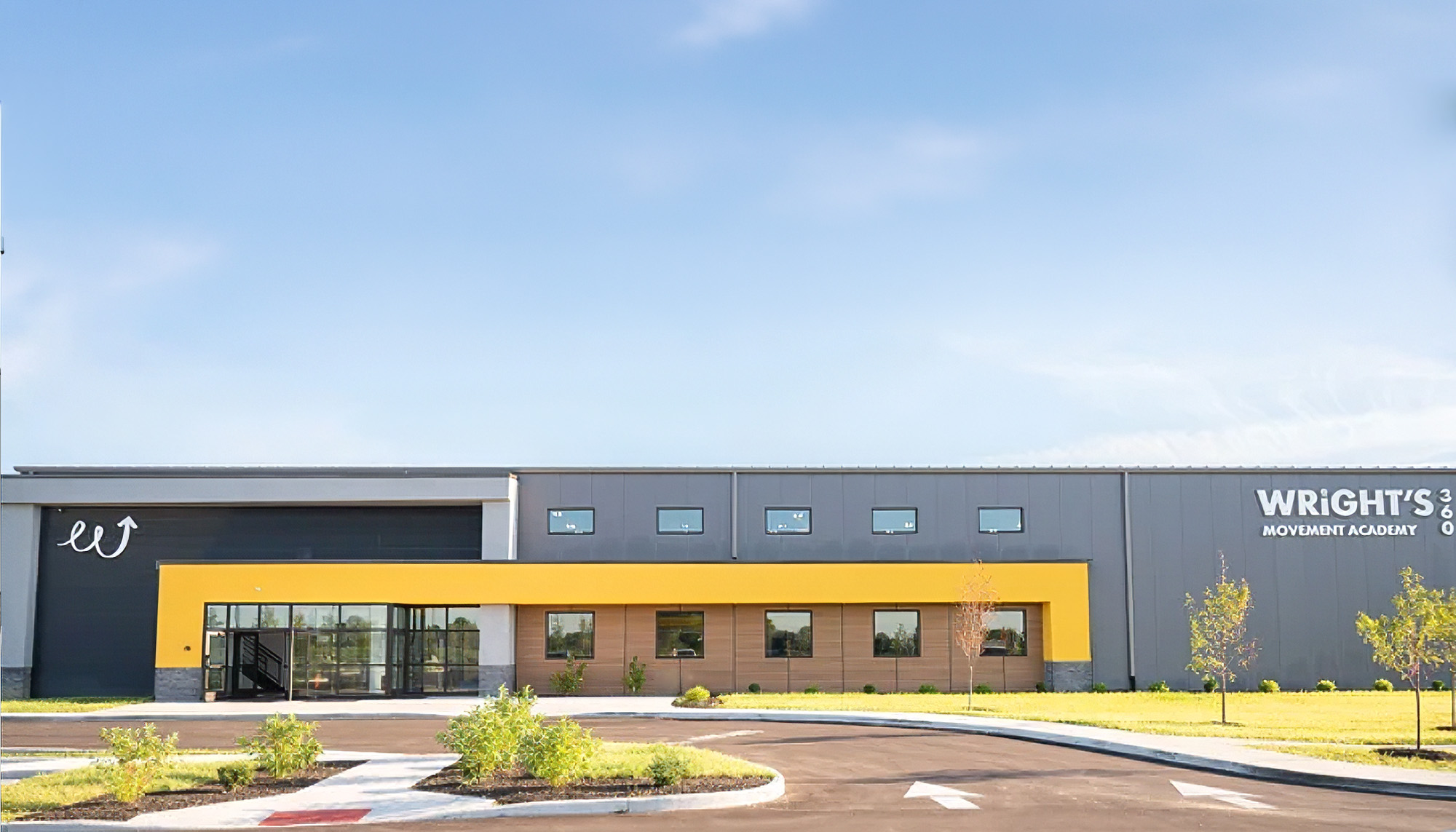 Modern commercial building with gray and yellow exterior, glass storefront entrance and landscaped drive-up access.