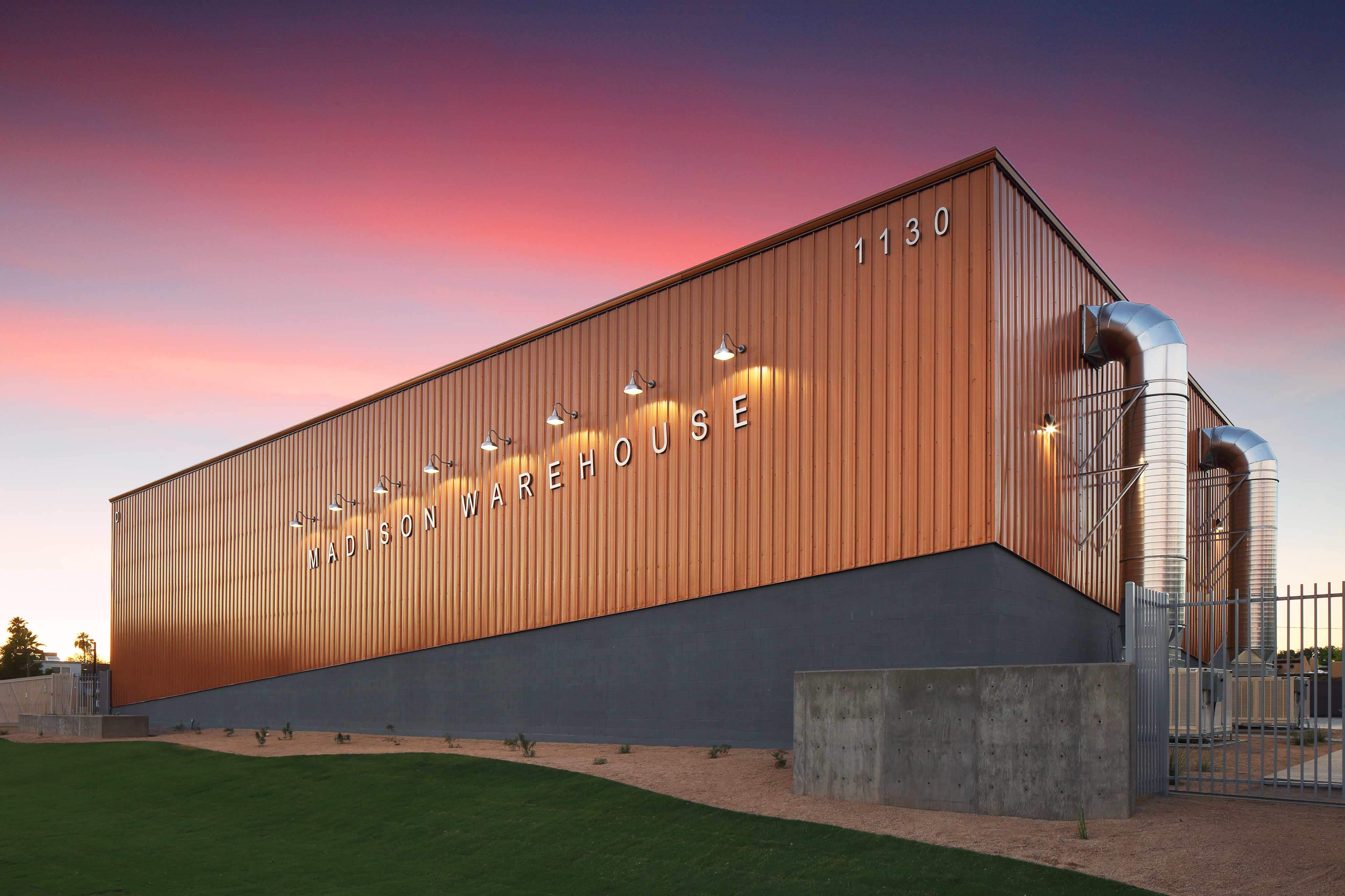 Modern metal warehouse building exterior at sunset with illuminated signage and exposed ductwork 