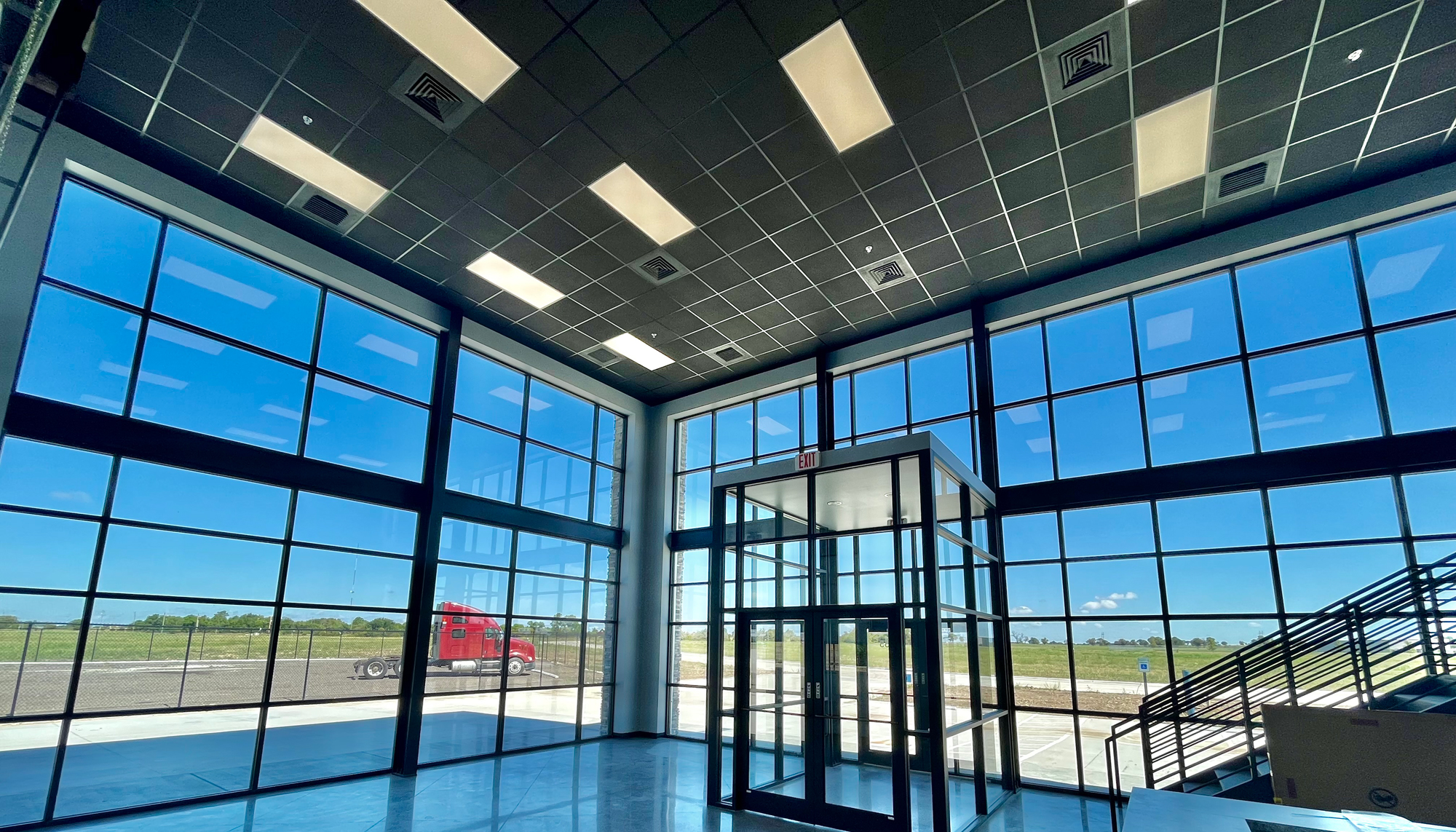 Interior lobby at the James Mason Enterprises facility featuring floor-to-ceiling glass walls, a glass entry vestibule and open staircase access.