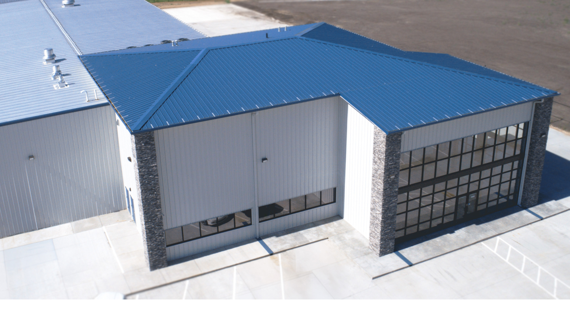 Aerial view of the James Mason Enterprises facility featuring a blue metal roof, large glass service doors and stone exterior accents.