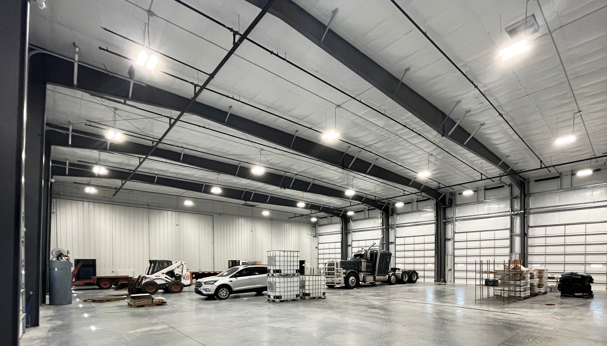Interior service bay at the James Mason Enterprises facility featuring a pickup truck, forklift, equipment storage and large vehicle access doors.