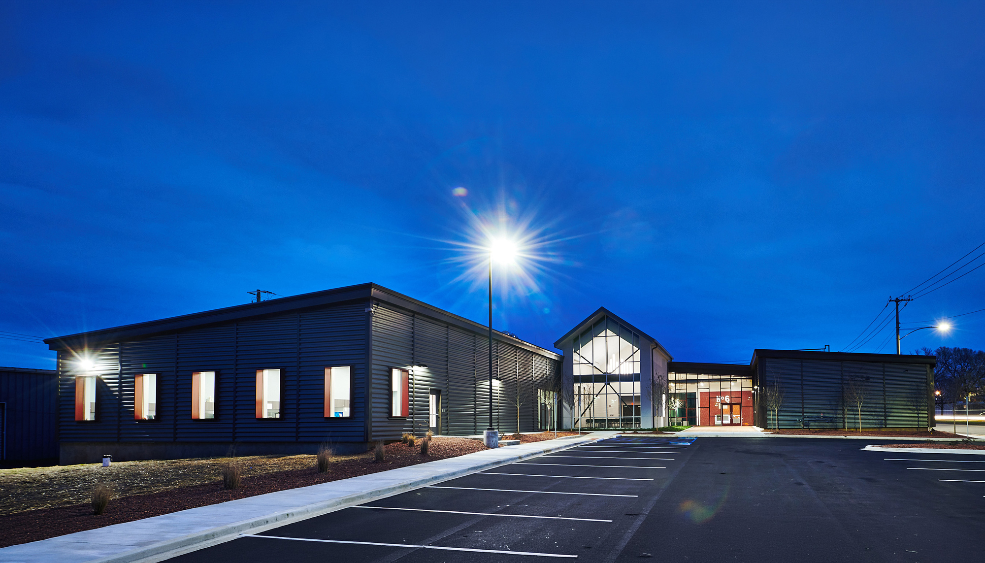 Exterior nighttime view of the Firehouse Shelter – New Facility featuring integrated residential and support spaces, welcoming entry design and a resilient community-focused environment developed to serve underserved individuals with dignity and long-term functionality.