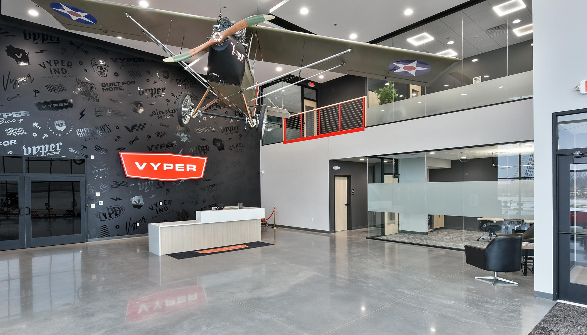 Modern VYPER lobby with polished gray floors, black and white walls, red accents, a reception desk and a suspended helicopter display overhead.