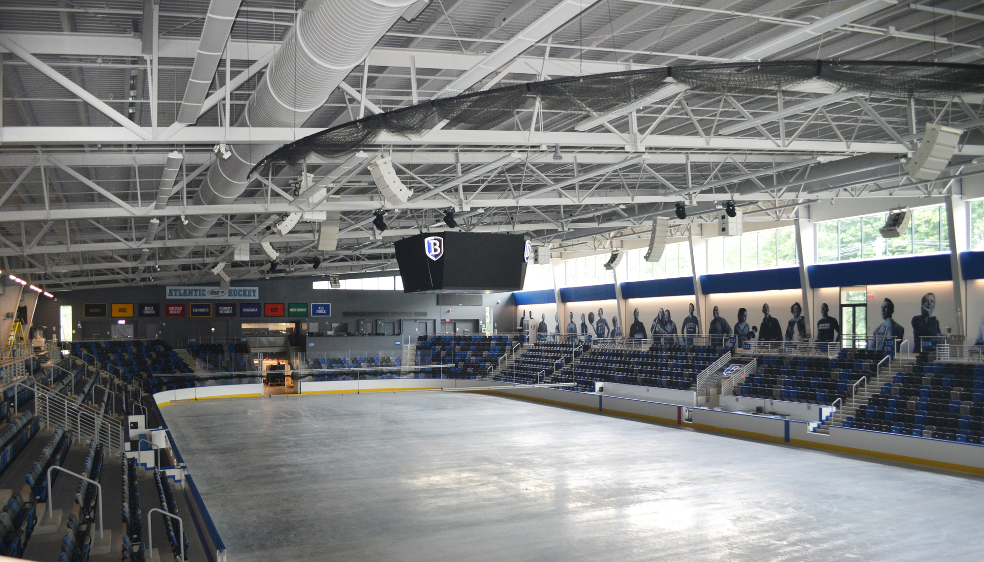 Interior view of Bentley University’s ice arena featuring flexible seating, exposed structural steel and scoreboard display.