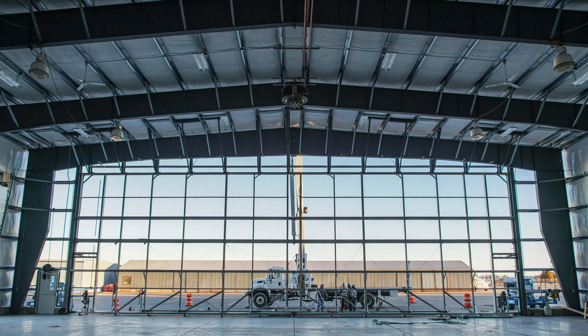 Interior view of the Maine Instrument Flight Corporate Hangar showing a large clear-span aircraft opening, integrated overhead systems and coordinated construction sequencing within a constrained aviation site.