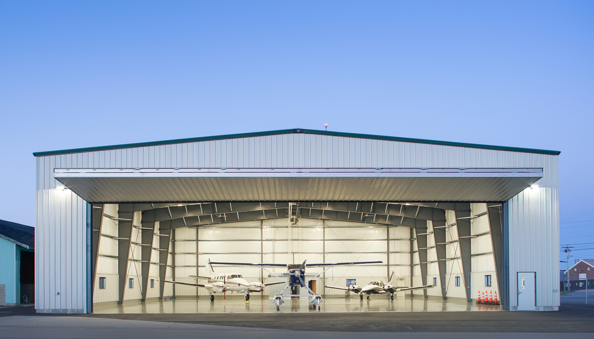 Front exterior view of the Maine Instrument Flight Corporate Hangar featuring a large clear-span aircraft opening and coordinated structural design developed to support efficient aviation operations within a constrained site.