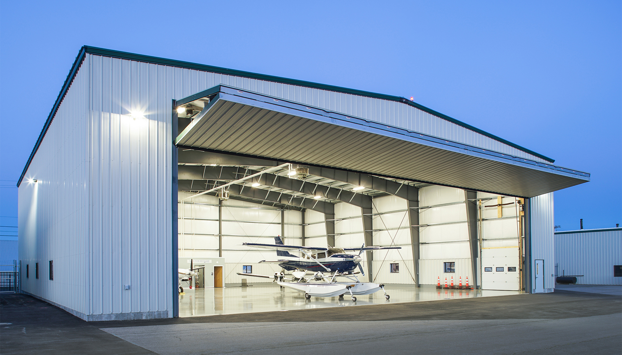 Angled exterior view of the Maine Instrument Flight Corporate Hangar featuring a clear-span aircraft opening, integrated lighting systems and coordinated structural design developed for efficient aviation access and safe site execution.