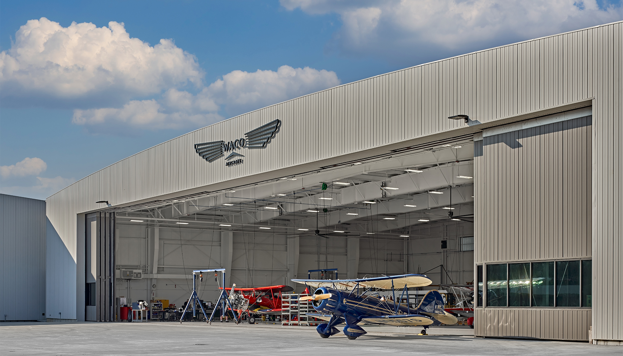 Exterior hangar view at the WACO Aircraft Corp. facility featuring a large clear-span aviation environment, integrated aircraft access and coordinated operational space designed to support manufacturing, assembly and customer engagement functions.