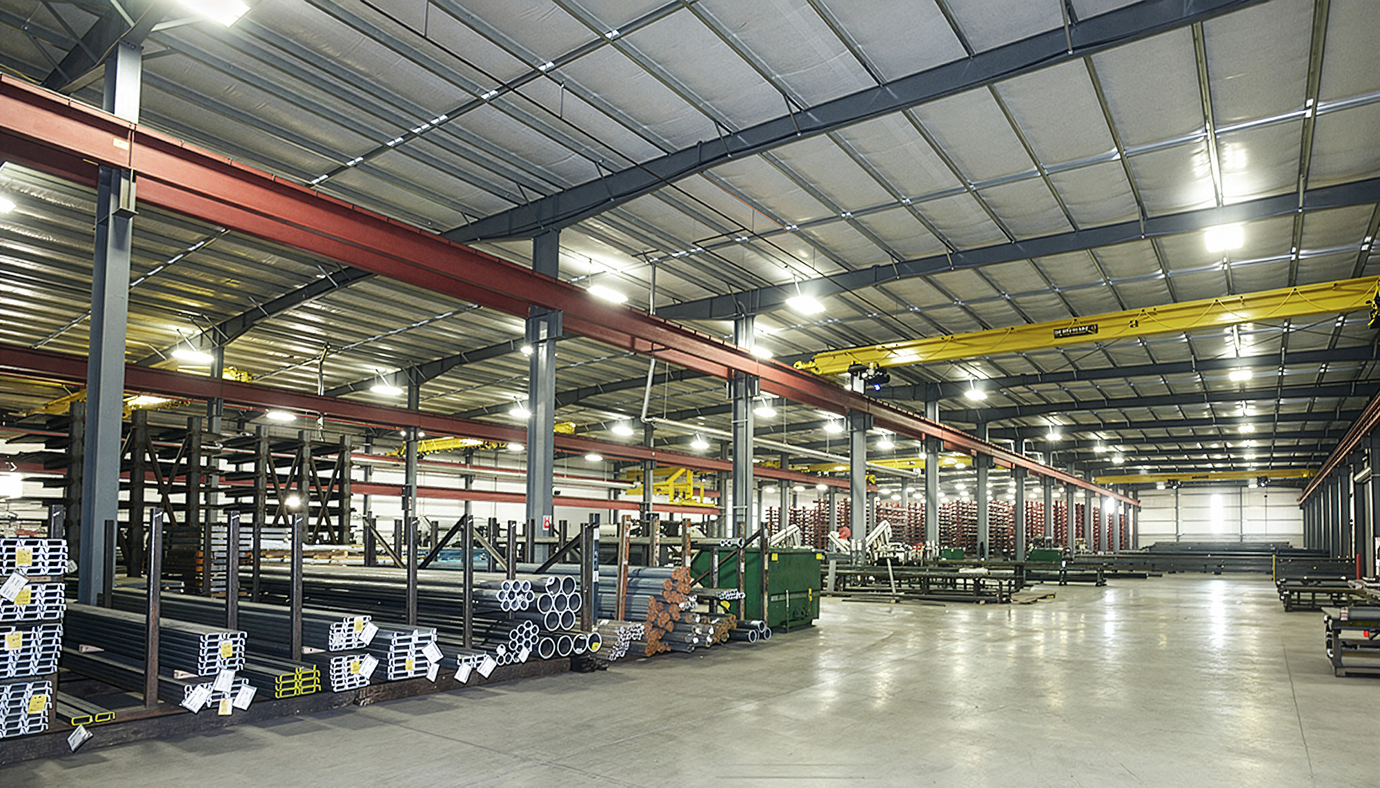 Industrial workspace at the Harbor Steel facility featuring overhead crane systems, steel storage racks and open operational floor space.