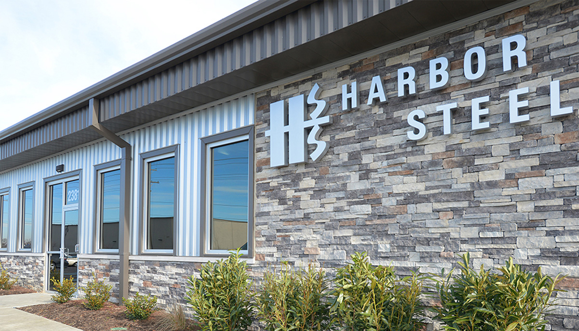 Exterior facade of the Harbor Steel facility featuring stone accents, metal wall panels and integrated storefront windows.