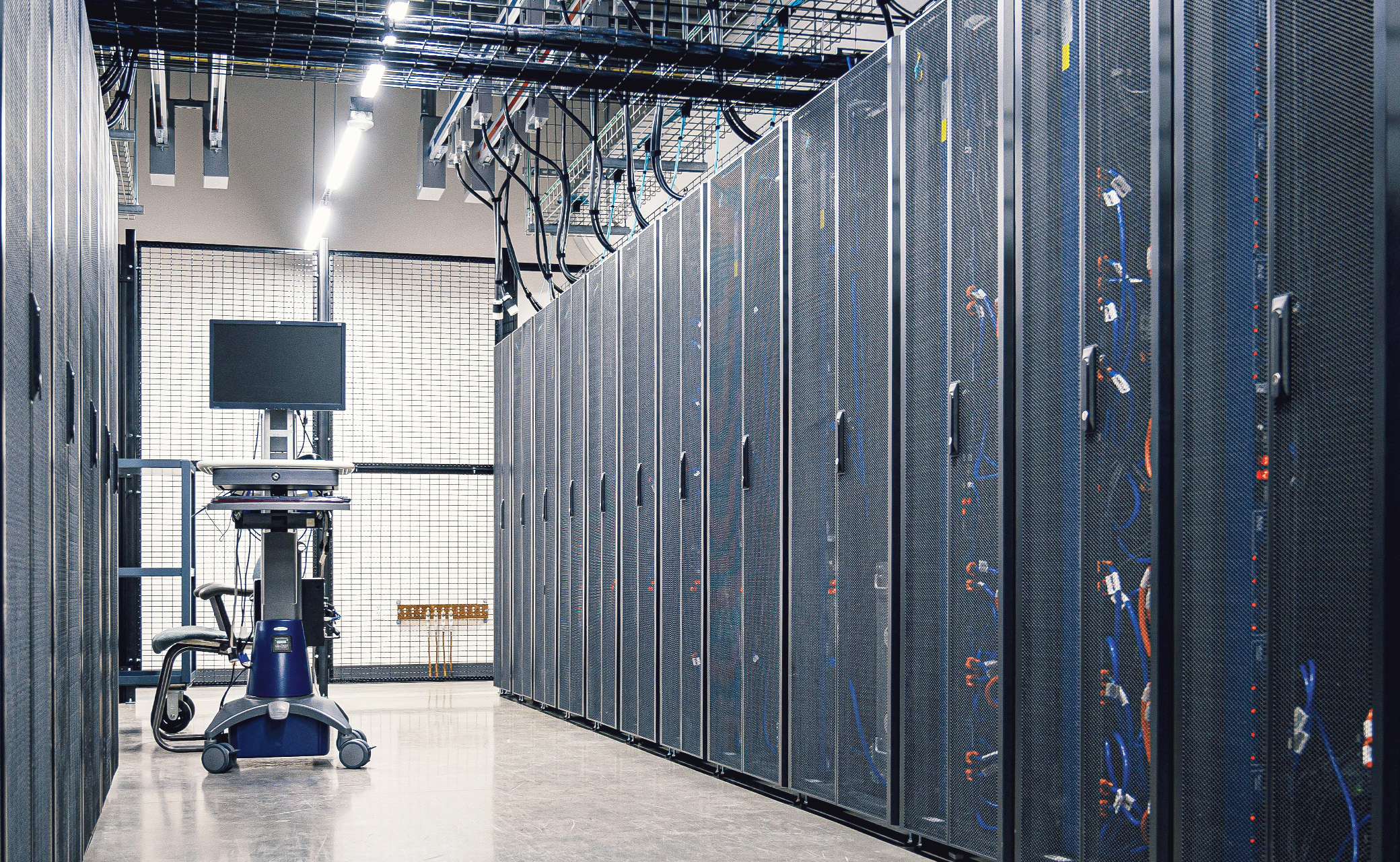 Close-up view of secure server cabinets with overhead cabling and mesh enclosure panels inside a modern mission critical data facility.