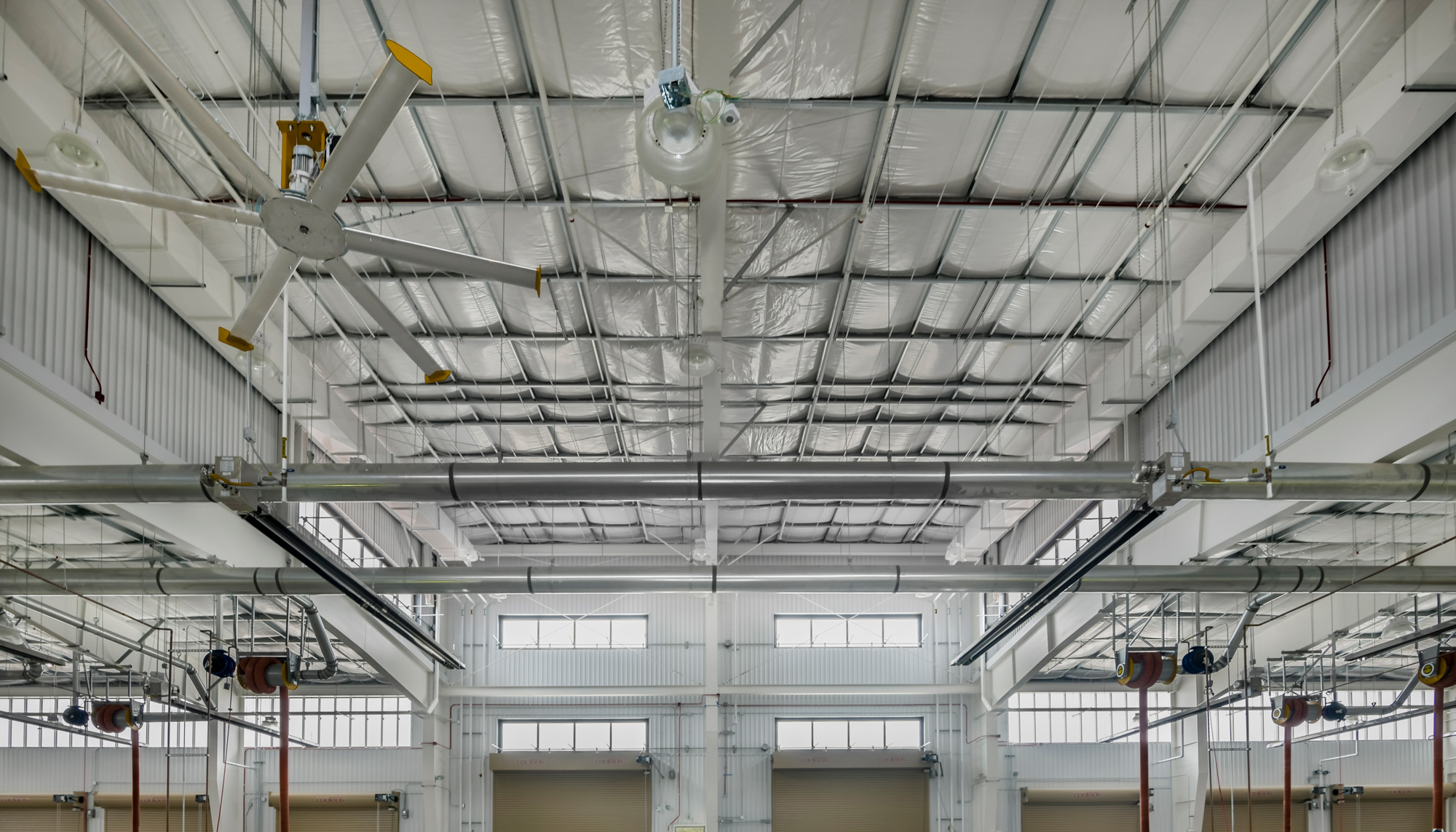 Interior view of the U.S. Navy Forklift Rework Facility featuring integrated overhead crane systems, insulated roof construction and open maintenance areas designed to support coordinated repair operations and workforce training.