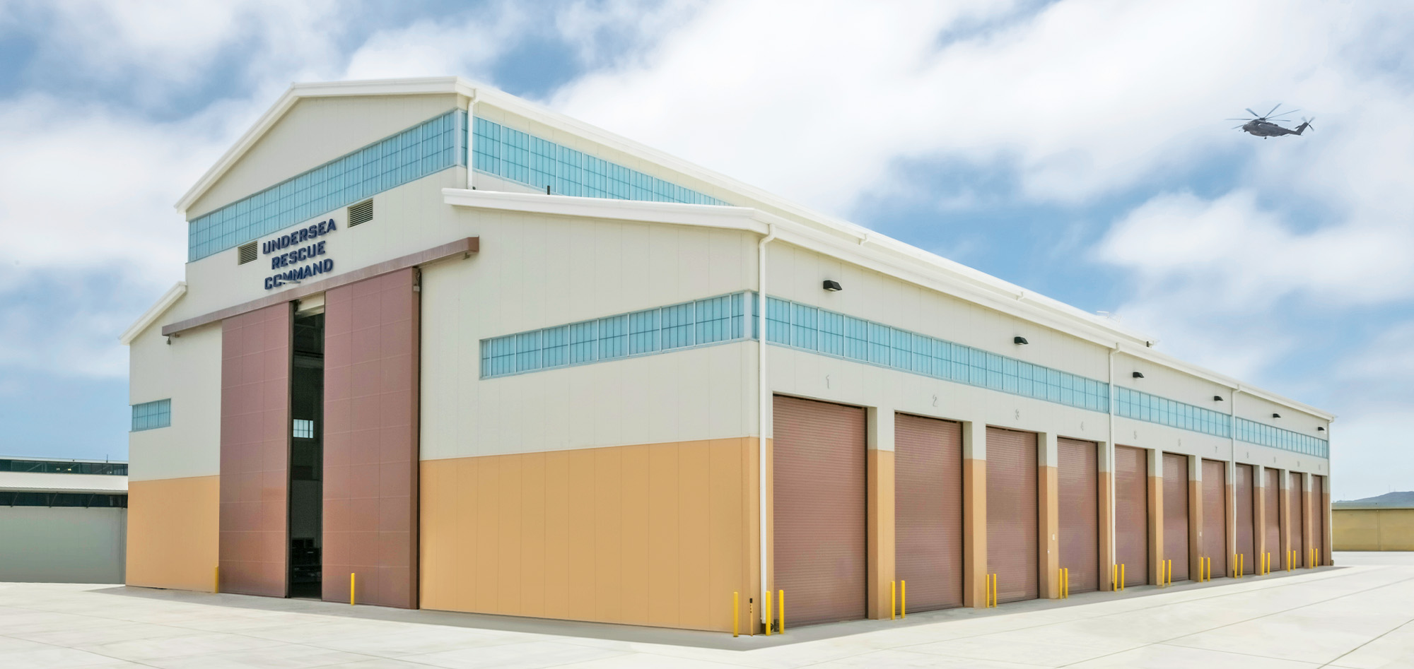 Large aircraft maintenance hangar with tan-and-white exterior, multiple vertical lift doors and clerestory windows designed to support aviation operations.