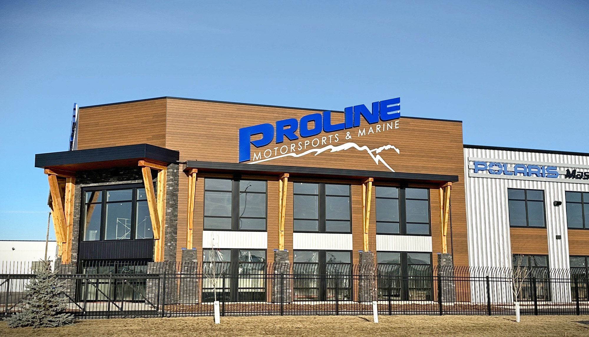 Front exterior of Proline Motorsports & Marine featuring wood-look wall panels, exposed timber columns, stone accents and large windows.
