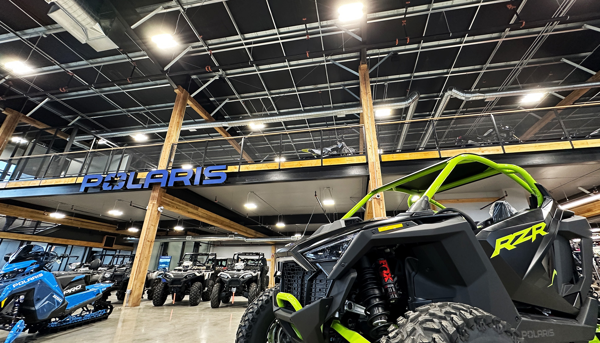 Polaris off-road vehicles and snowmobiles displayed inside Proline Motorsports & Marine beneath an exposed ceiling structure with timber columns and a mezzanine.