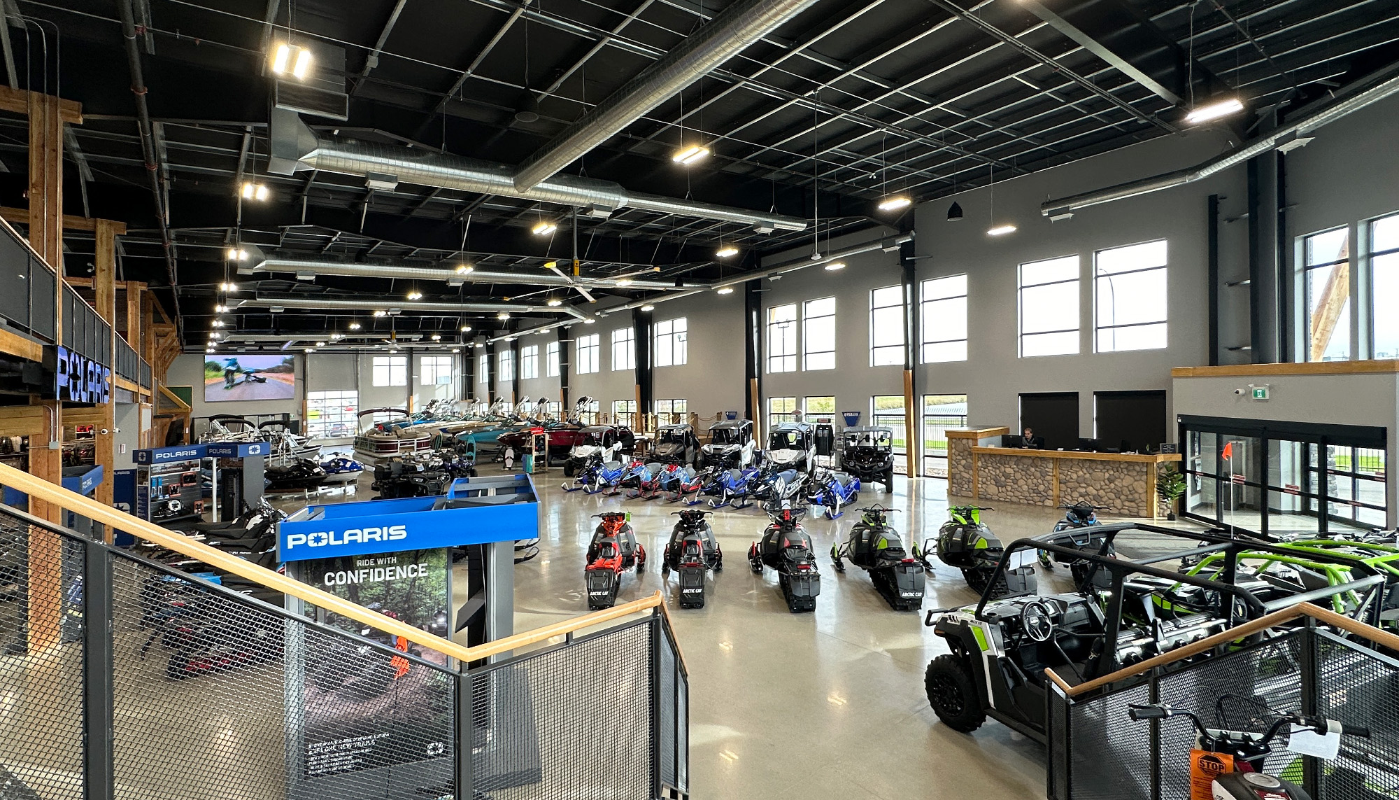 Elevated view of the Proline Motorsports & Marine showroom featuring rows of snowmobiles, off-road vehicles and boats beneath a high ceiling with exposed framing.