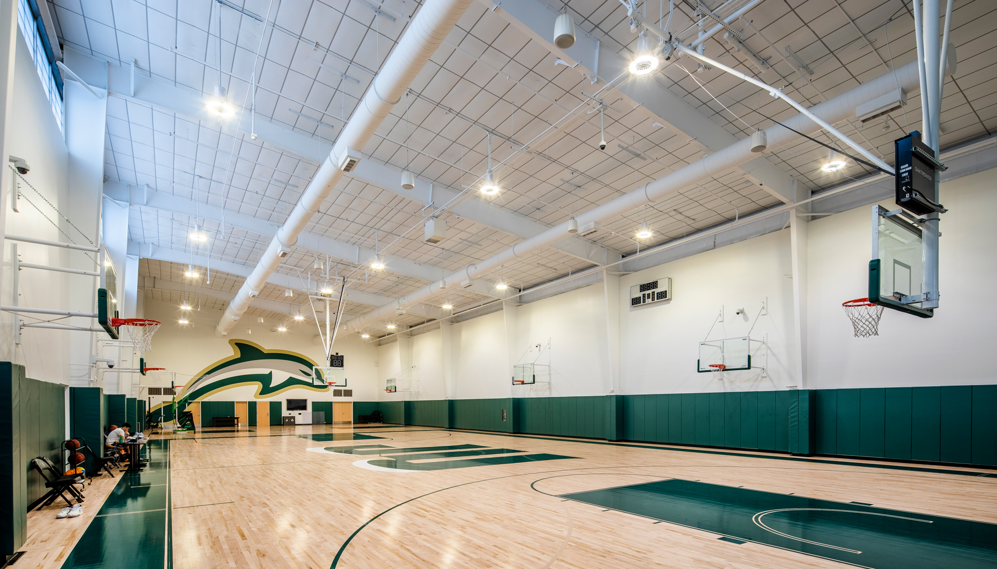 Indoor basketball practice court at the Jacksonville University Basketball Performance Center featuring hardwood flooring, green court accents and a large dolphin mascot graphic.