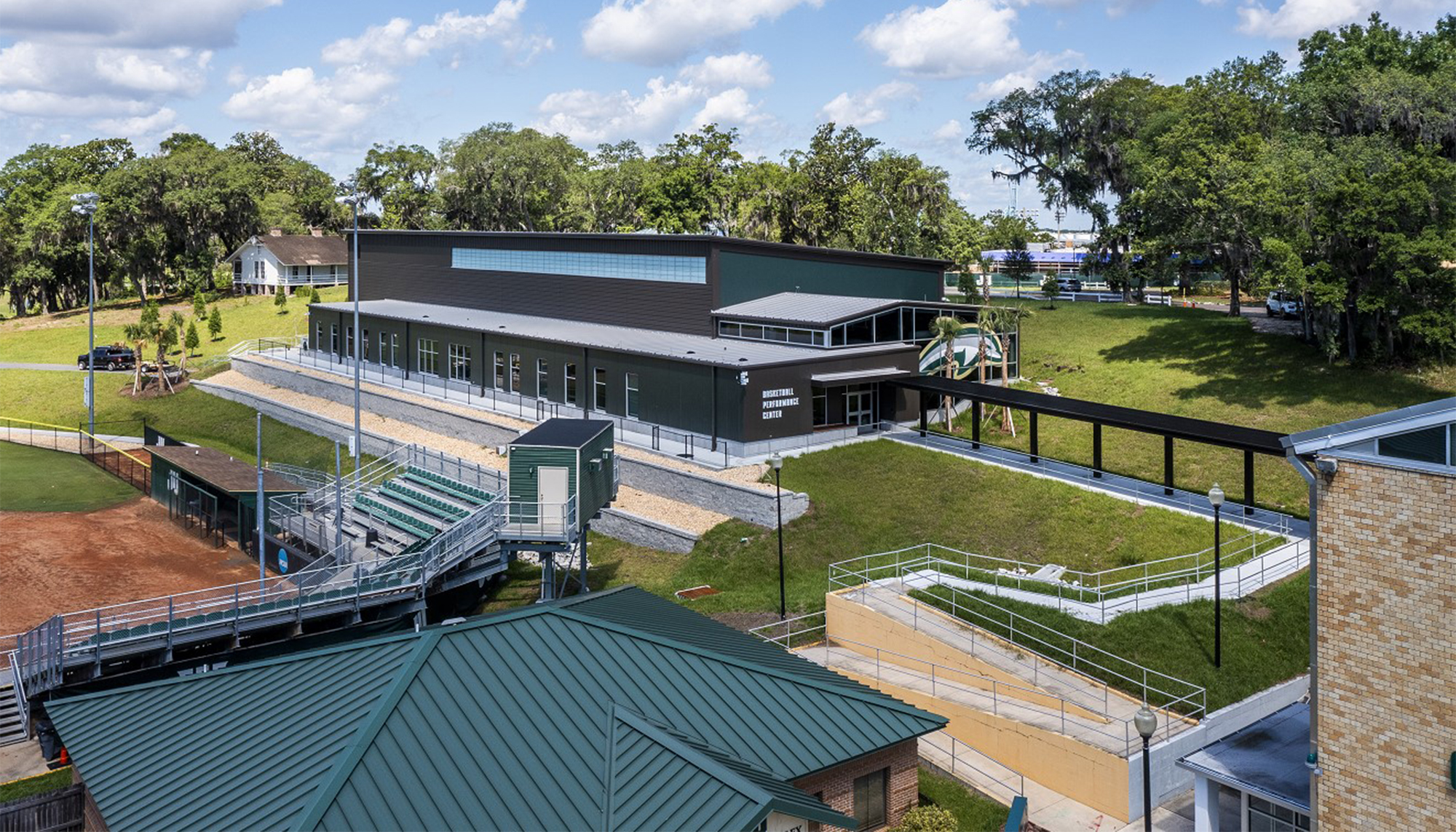 Exterior view of the Jacksonville University Basketball Performance Center featuring elevated walkways, tiered landscaping and a green metal building exterior.