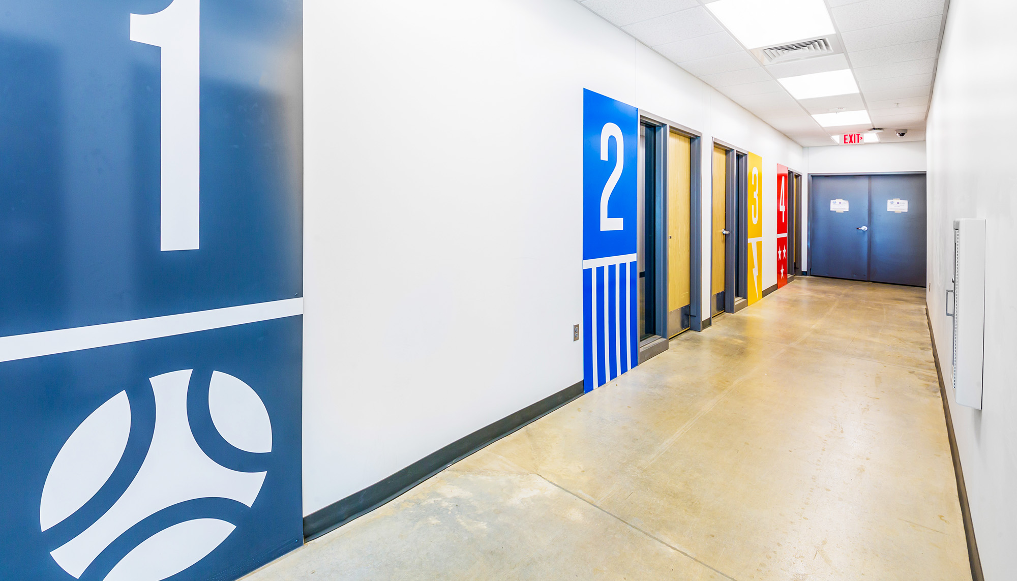 Sports complex corridor featuring team locker room access, wayfinding graphics and modern athletic facility design.