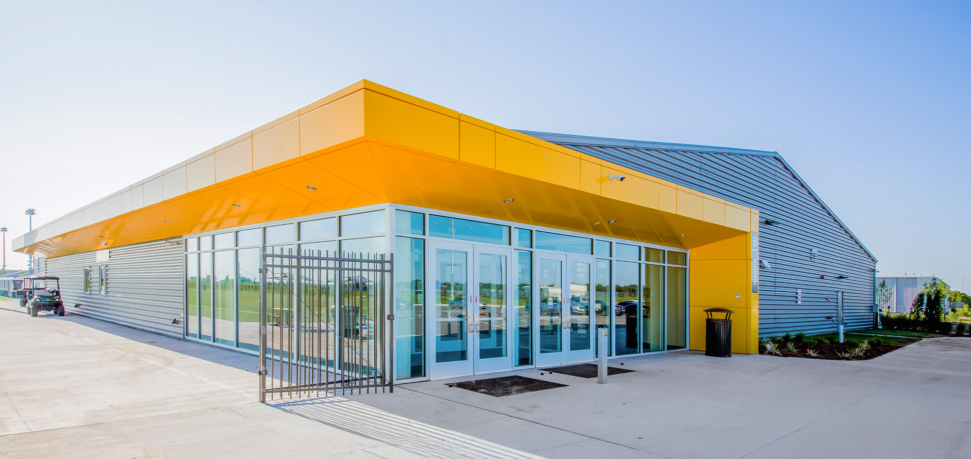 Steel building entrance with bright yellow metal canopy, silver-gray siding and blue-tinted glass doors.