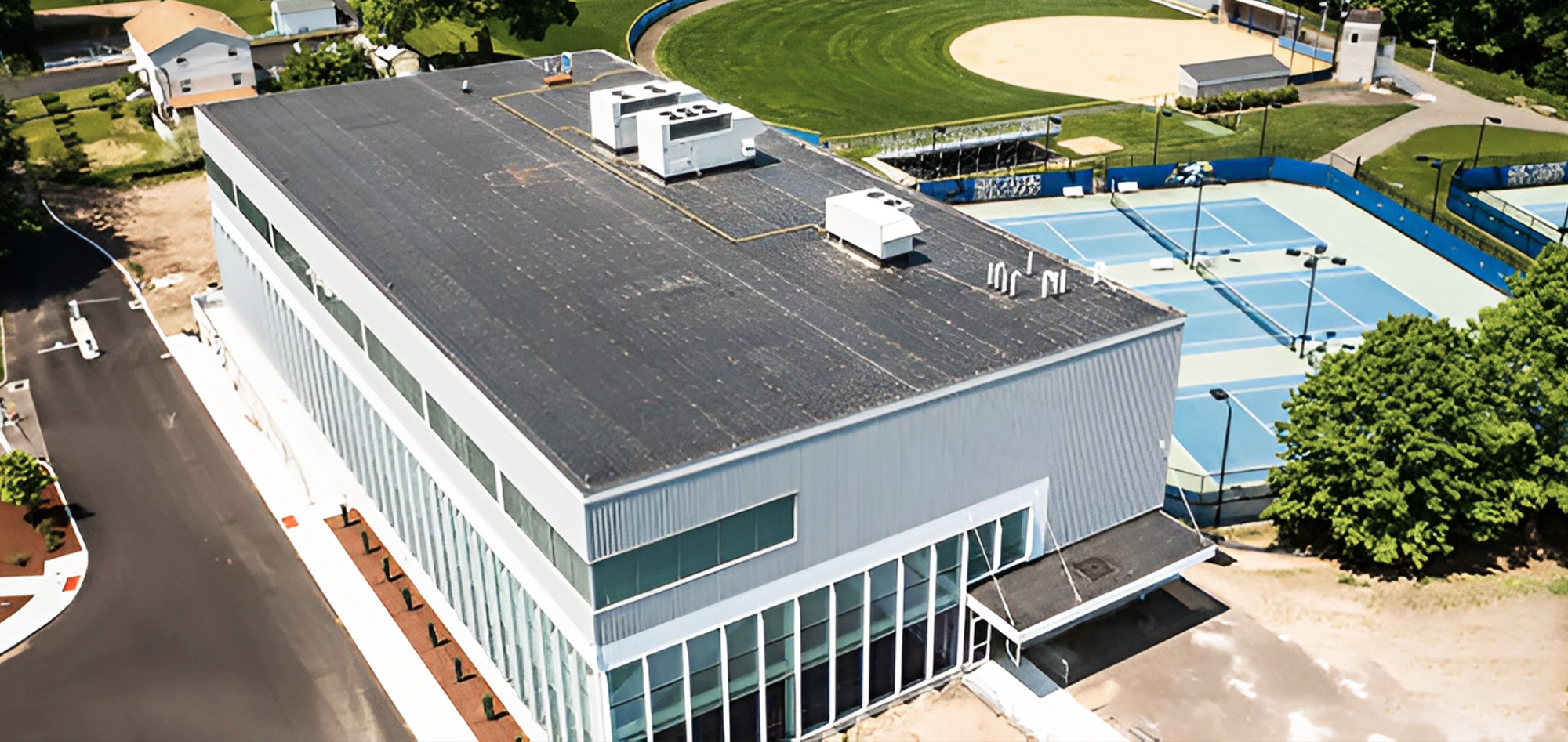 Athletic facility featuring metal wall panel systems, curtain wall glazing and recreation center construction adjacent to outdoor sports courts.