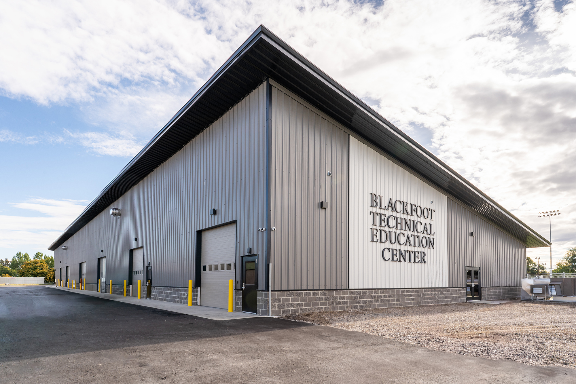 Modern technical education facility with light gray metal panel facade, overhead service bays and clean industrial design beneath a bright sky with scattered clouds.