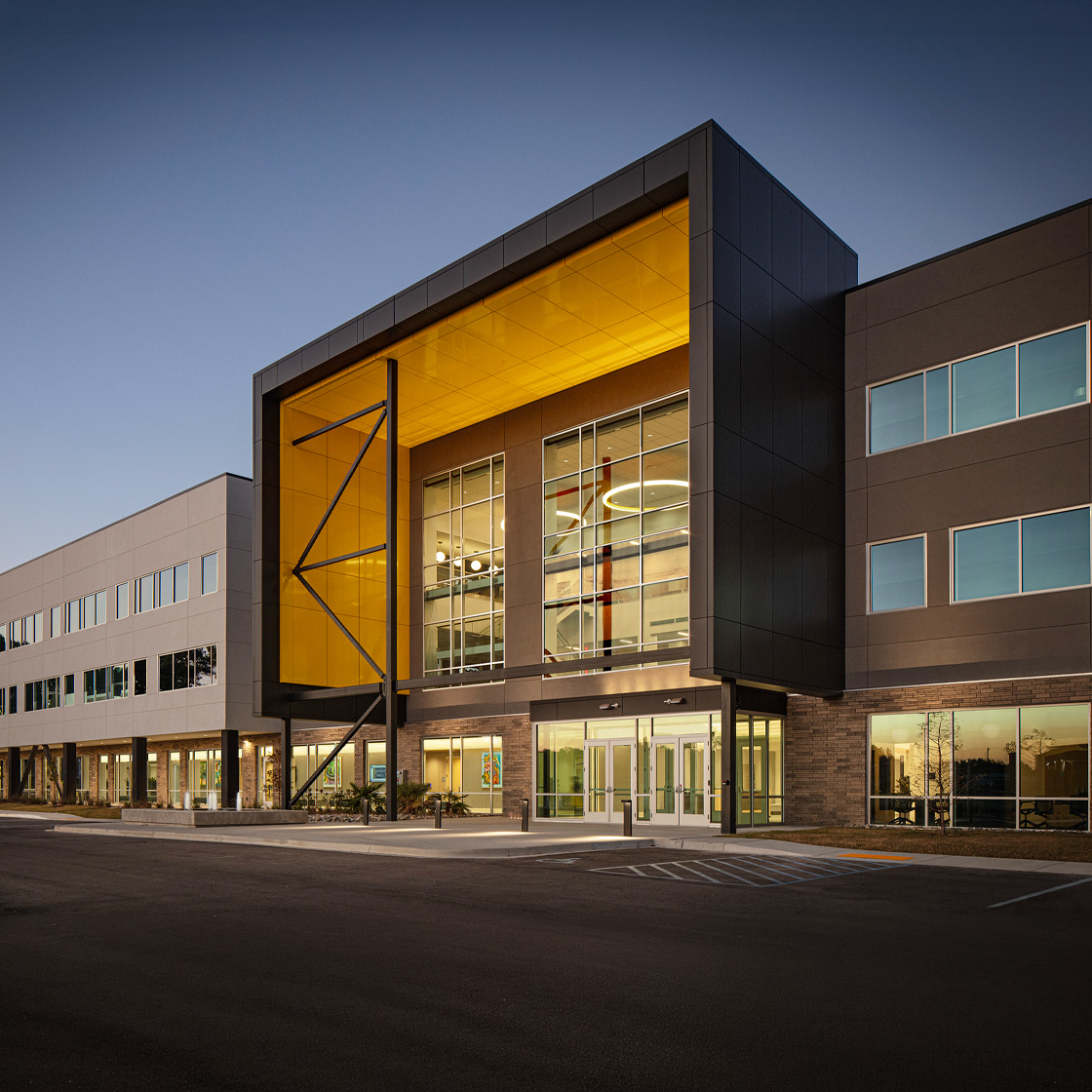 Contemporary office building with bold black metal framing, dramatic illuminated gold entry feature and expansive glass facade at dusk.
