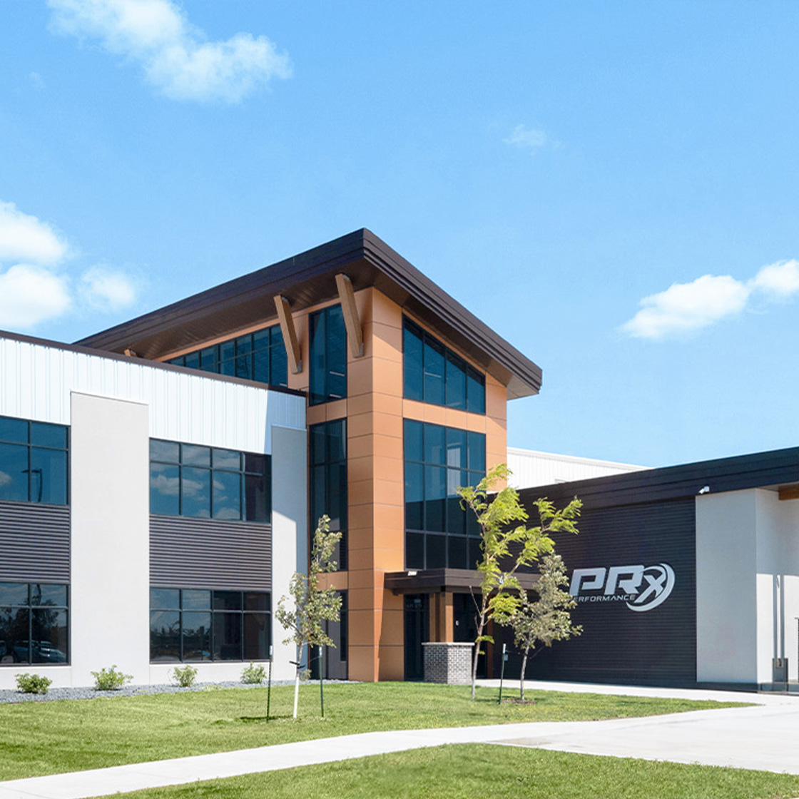 Contemporary corporate office building with warm copper-toned entry tower, expansive glass frontage and clean modern landscaping beneath a bright blue sky.