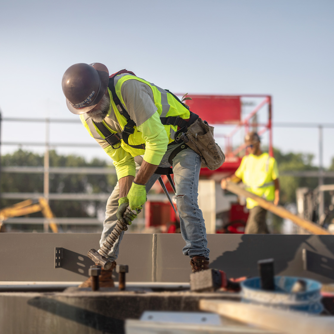 Construction worker in high-visibility safety gear securing steel connections on an active job site with structural framing in the background.